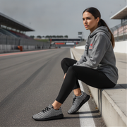 Woman sitting on a race track wearing a gray hoodie and black checkered shoes.