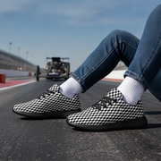 Person wearing checkered shoes on a race track with a truck in the background