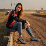 Woman sitting on a dirt track wearing a red and black jacket, blue jeans, and checkered shoes.