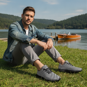 Man sitting on grass by a lake wearing checkered shoes