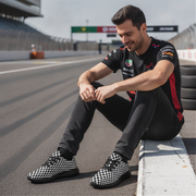 Man sitting on a race track wearing checkered sneakers and a branded shirt.