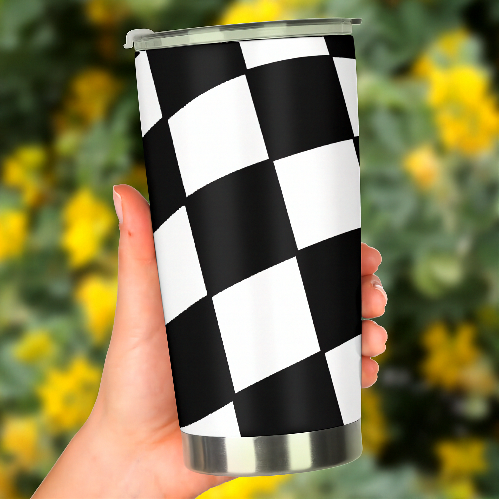 Checkered pattern tumbler held in a hand with a blurred yellow flower background