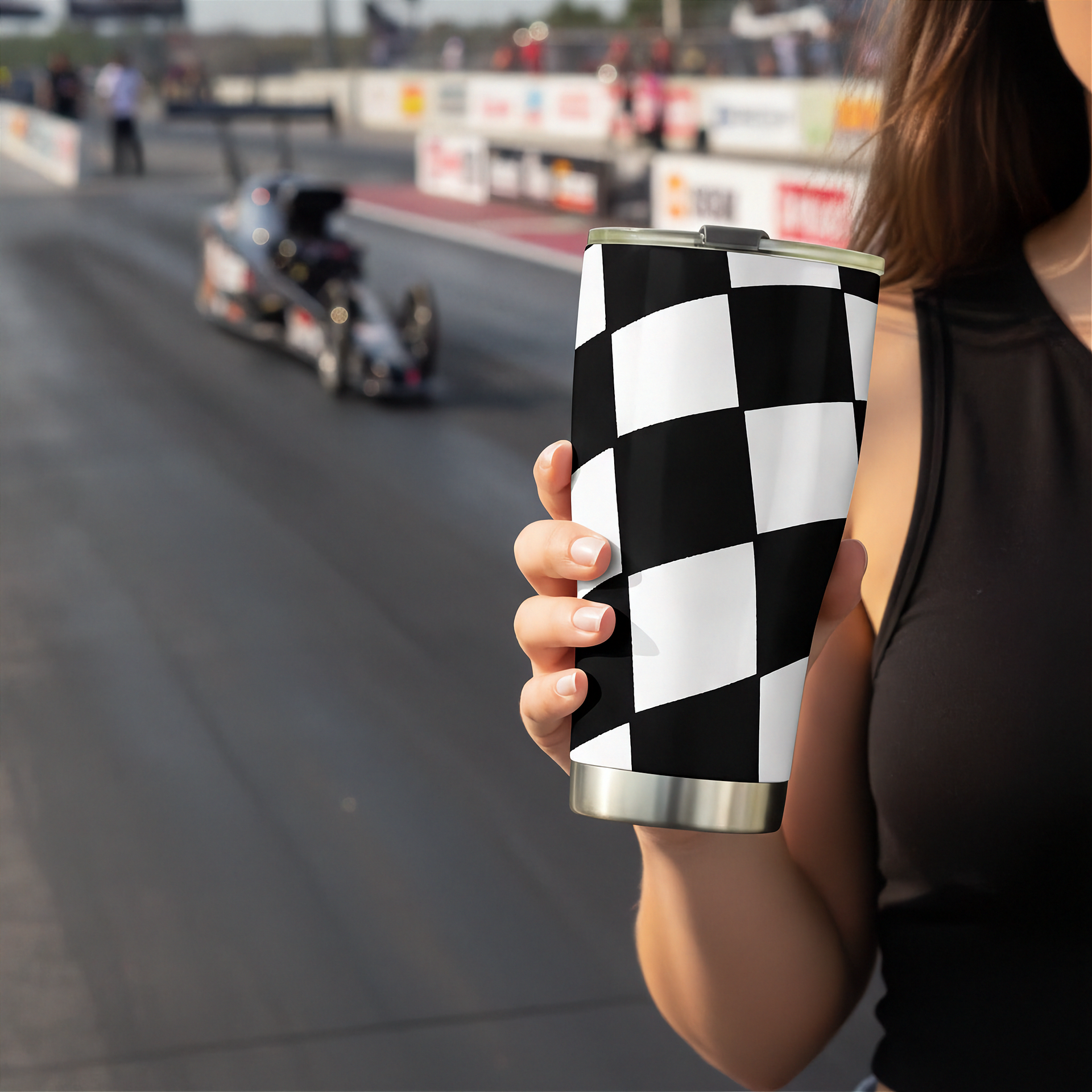 Woman holding a checkered pattern tumbler with a blurred race track in the background