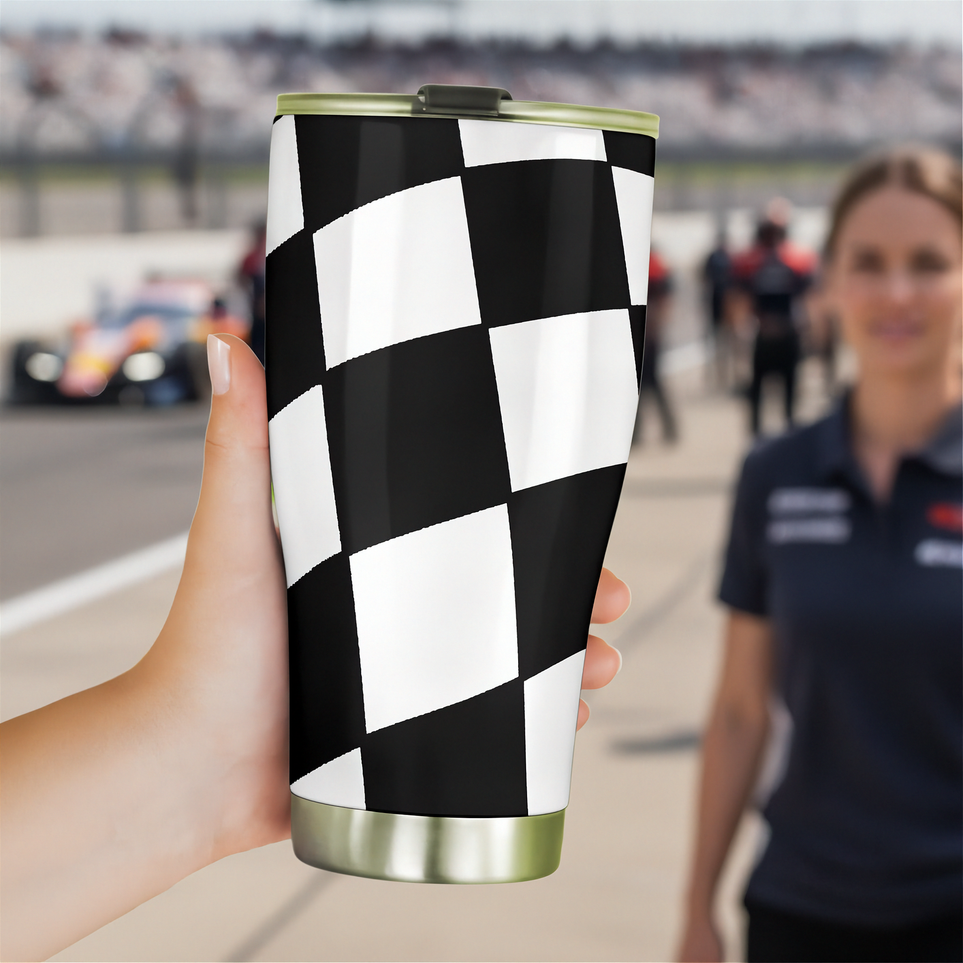 Checkered pattern tumbler held by a hand with a blurred race track background
