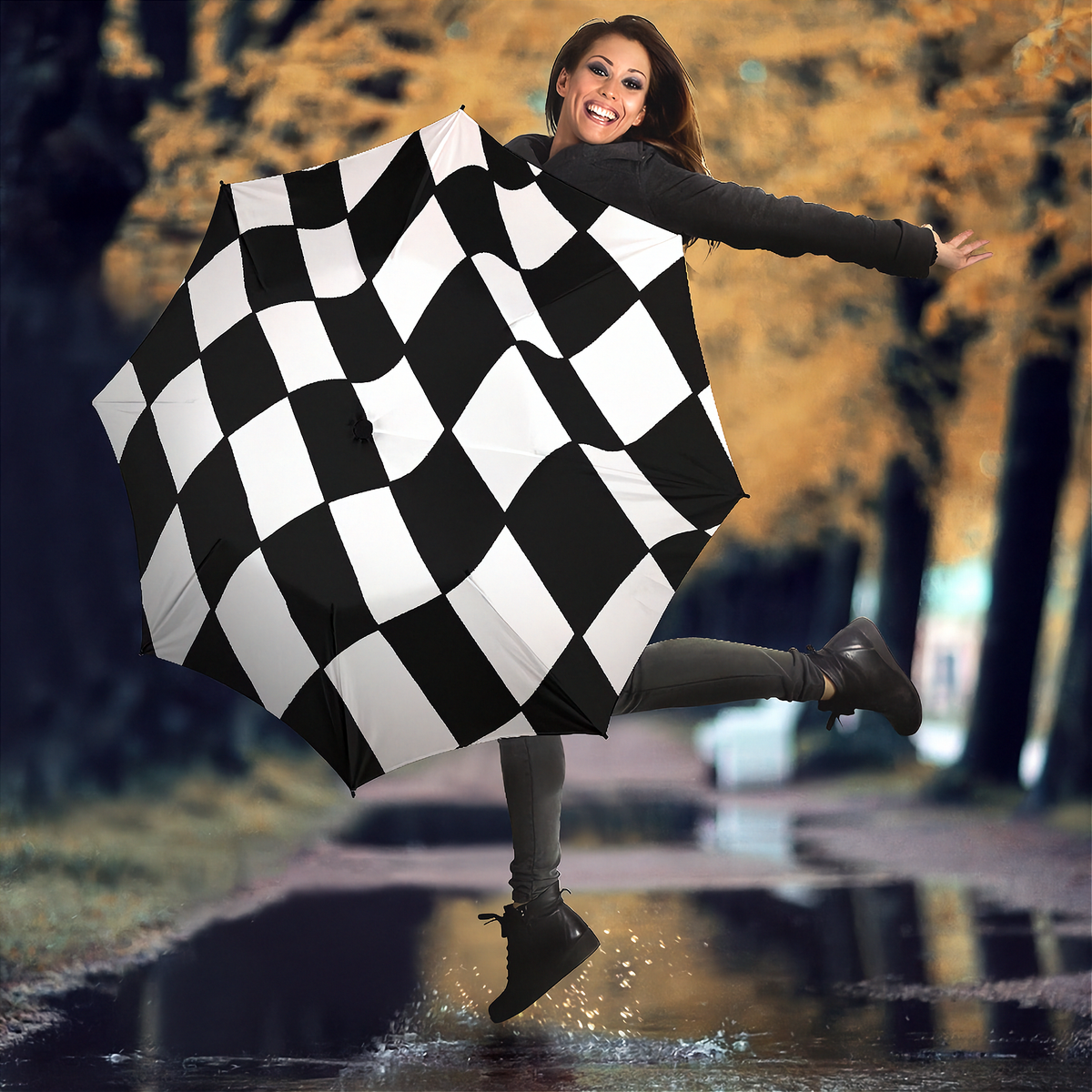A woman stands on a wet street holding a large black-and-white checkered umbrella. She wears a dark rain jacket, dark leggings, and black boots.