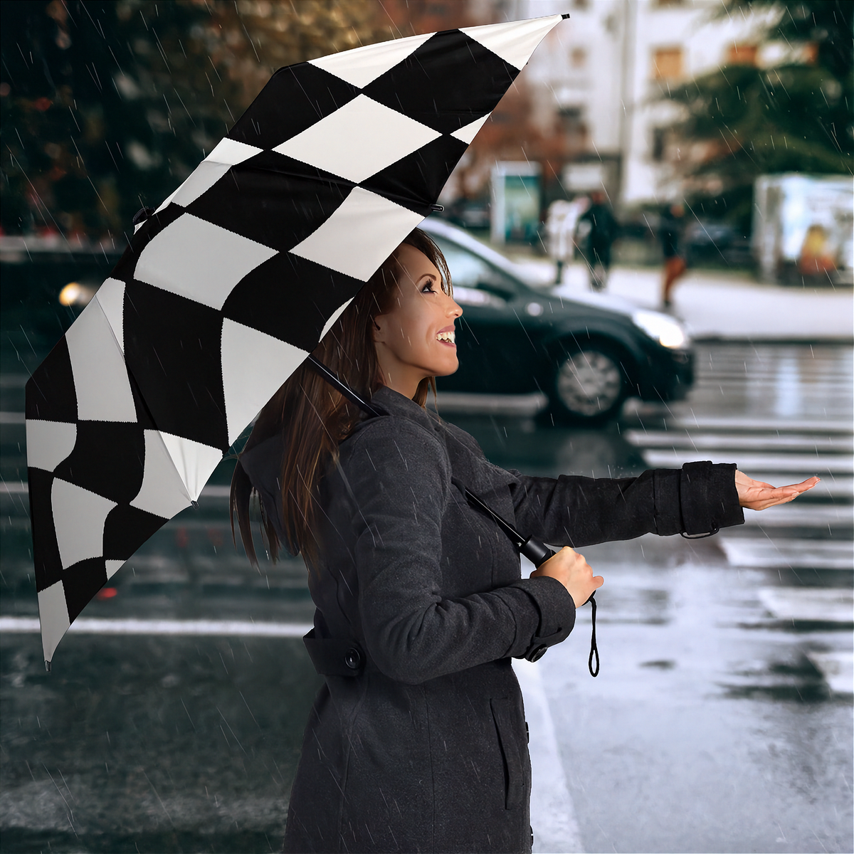 A woman in a dark gray coat stands in the rain on a city street holding a large black-and-white checkered umbrella, with a blurred car and city background behind her.