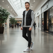 Man standing in a modern mall wearing a black vest and white shoes.