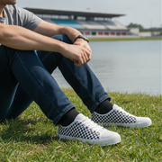 Person wearing checkered shoes sitting on grass by a lake
