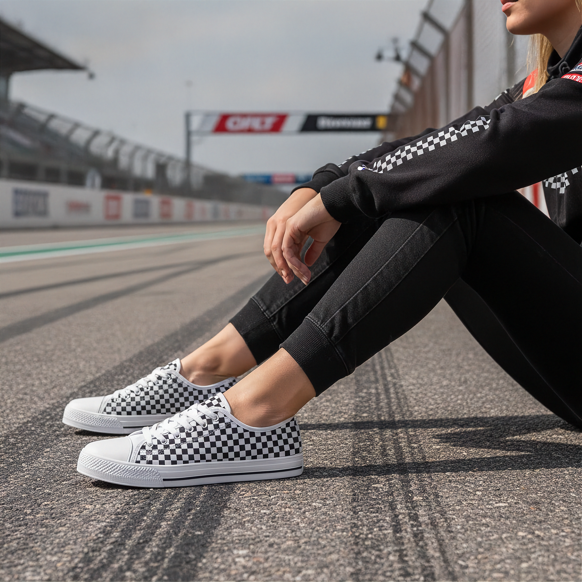 Woman wearing checkered shoes sitting on a race track with racing-themed background