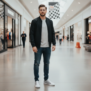 Man standing in a modern mall wearing a black jacket, white shirt, and jeans.