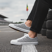 Person wearing white sneakers with black checkered pattern on a racetrack.