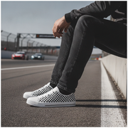 Person wearing checkered sneakers sitting on a race track with cars in the background