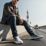 Man sitting on a concrete barrier by a race track wearing checkered sneakers.