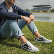 Person sitting on grass wearing checkered sneakers with a lake and stadium in the background