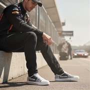 Person wearing checkered racing shoes sitting on a concrete ledge with a blurred race track background.