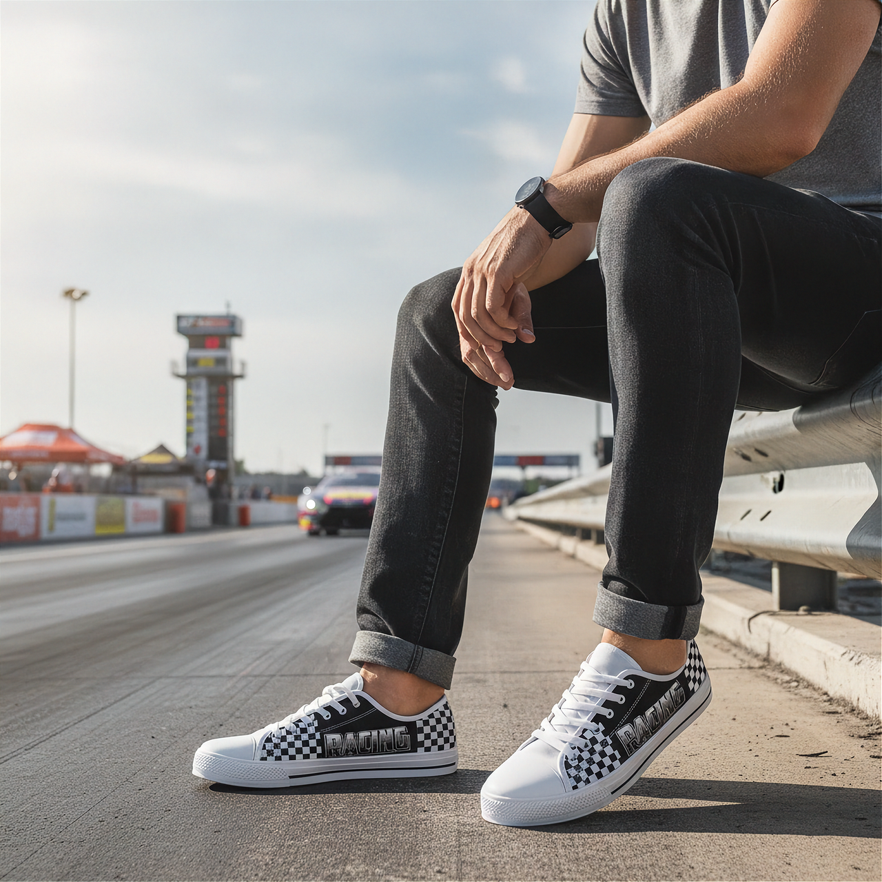 Person wearing checkered low top shoes sitting on a guardrail by a race track.