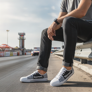 Person wearing checkered low top shoes sitting on a guardrail by a race track.