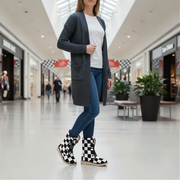 Woman wearing a gray cardigan, white shirt, blue jeans, and checkered boots in a mall.