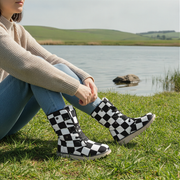 Person wearing checkered boots sitting by a lake