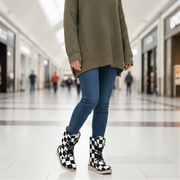 Person wearing a green sweater, blue jeans, and checkered boots in a mall.
