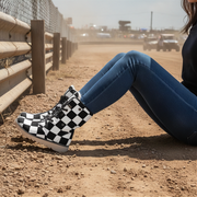 Woman sitting on a dirt track wearing checkered boots and blue jeans.