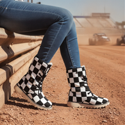 Person wearing checkered boots sitting on a wooden bench with a dirt track in the background