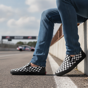 Person wearing checkered shoes on a race track with a car in the background