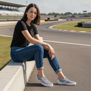 Woman sitting on a race track wearing black t-shirt, blue jeans, and checkered shoes.