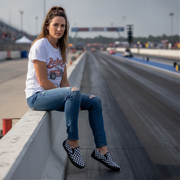 Woman sitting on a barrier at a race track wearing a white t-shirt and blue jeans and checkered shoes