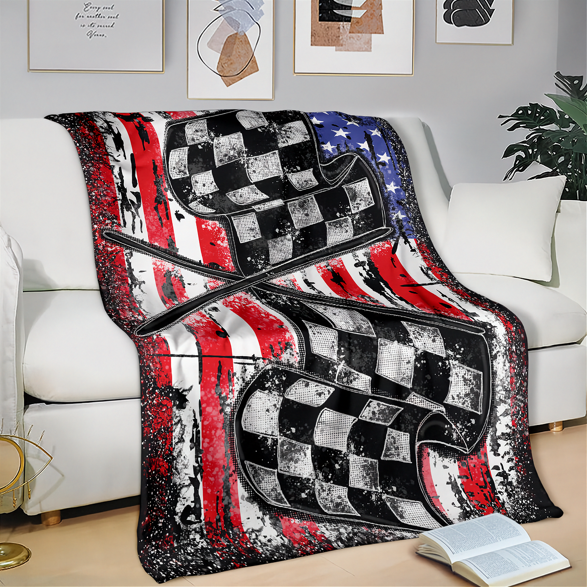 A throw blanket draped over a white sofa in a living room setting, featuring a distressed American flag design with red, white, and blue stripes and large black-and-white checkered racing flags layered across the front.