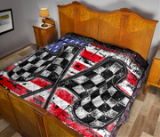 A quilted bedspread featuring a large checkered flag motif over a distressed American flag pattern, shown on a bed in a bedroom setting.