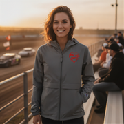 Woman wearing a gray jacket with a red racing daughter heart design at a race track during sunset.