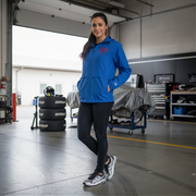 Woman in a blue jacket with a red racing daughter heart design standing in a garage with tires and tools in the background