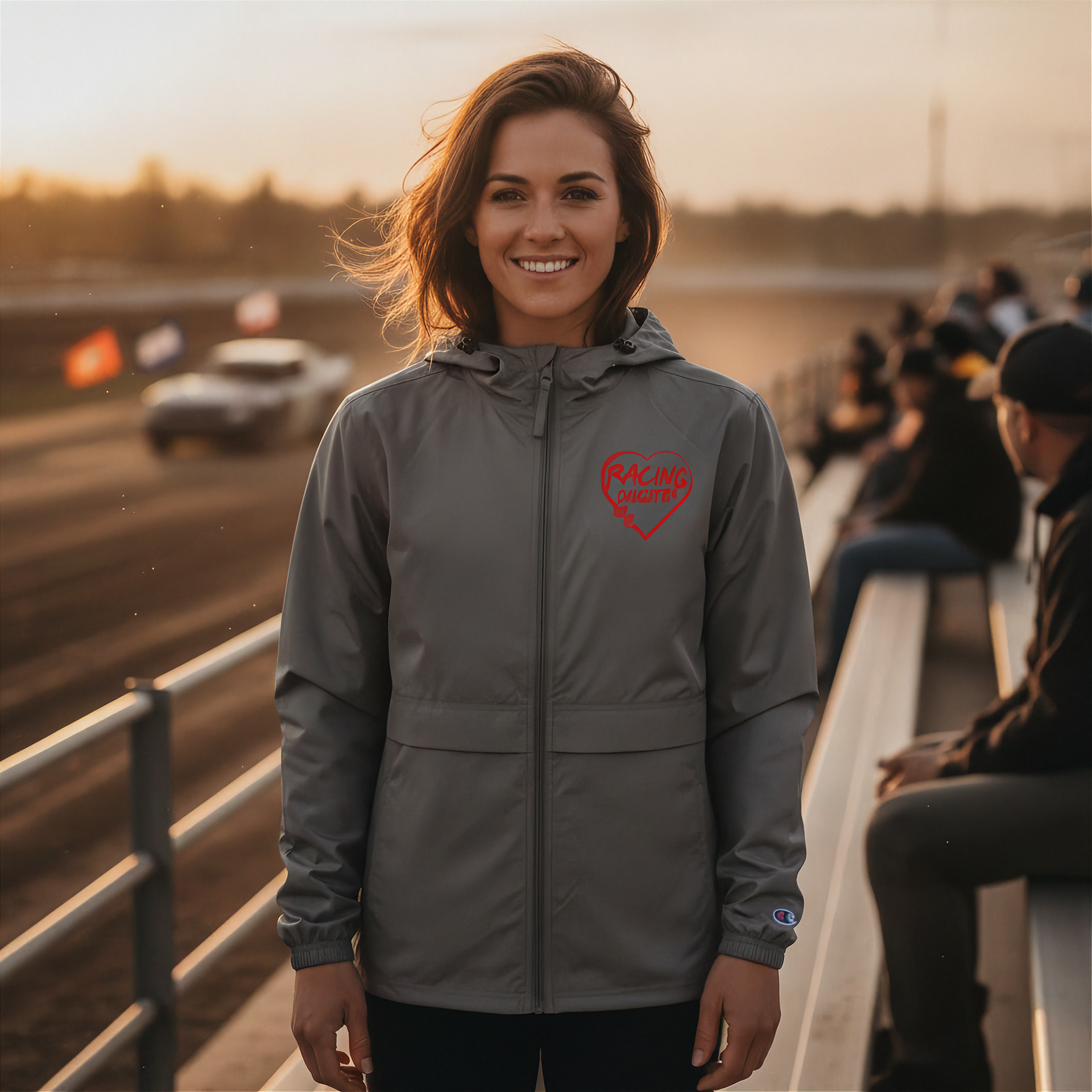 Woman wearing a gray jacket with a red racing daughter heart design at a race track.