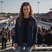 Woman standing on a race track wearing a navy jacket with a red logo, surrounded by people and racing equipment.