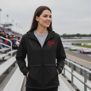 Woman wearing a black jacket with a red racing daughter heart design at a race track.