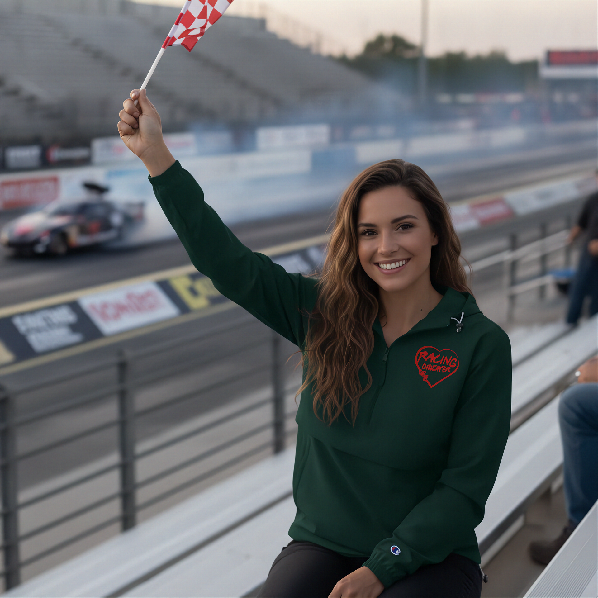 Woman in green shirt holding a flag with a red racing daughter heart design at a race track
