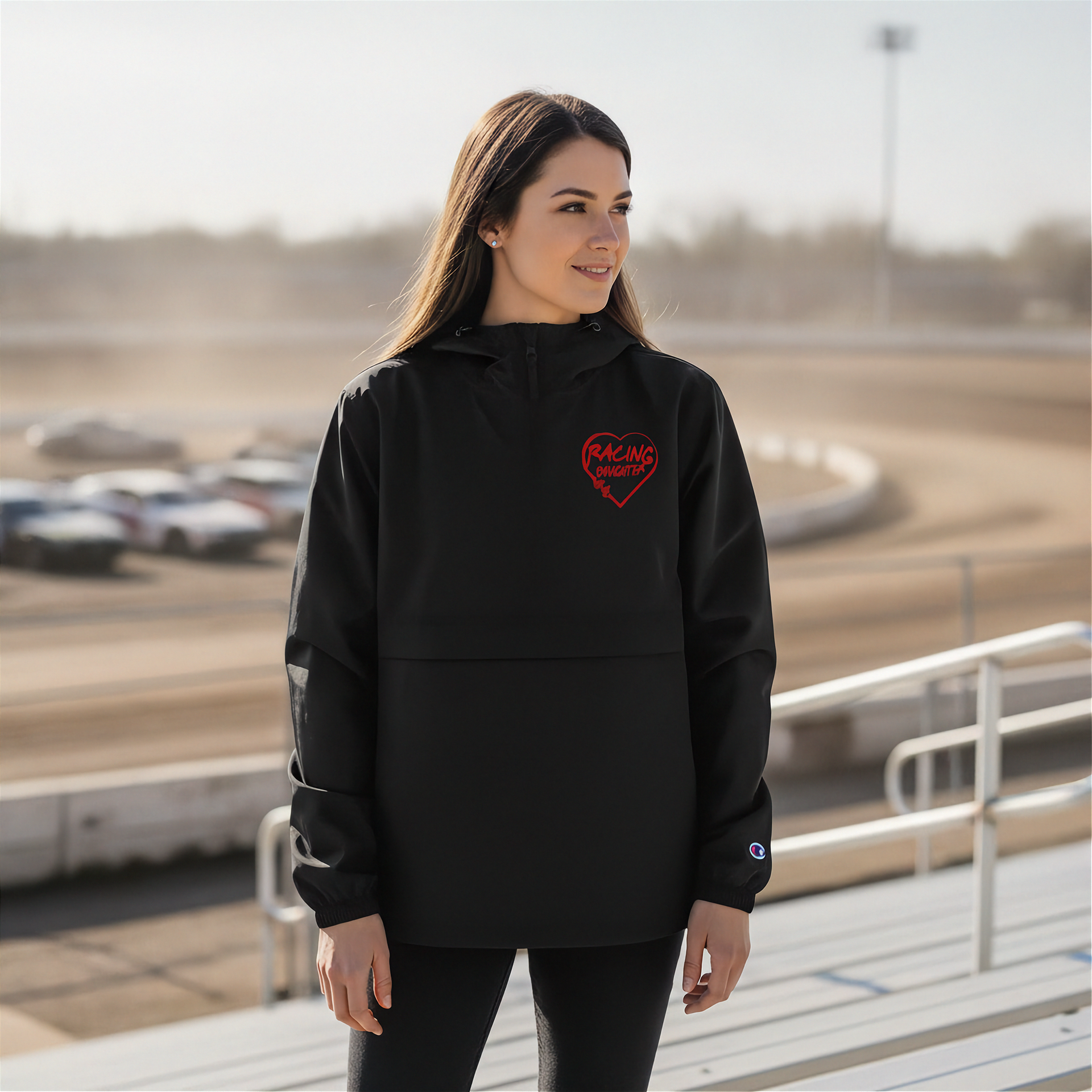 Woman wearing a black hoodie with a red racing daughter heart design at a race track.