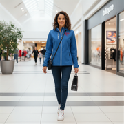 Woman in a blue jacket with a red racing daughter heart design walking through a shopping mall.