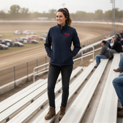 Woman wearing a navy jacket with a red racing daughter heart design, standing on bleachers at a race track.