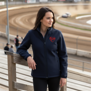 Woman wearing a navy blue jacket with a red racing daughter heart design at a race track.