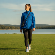 Woman in a blue jacket with a red racing daughter heart design walking on grass with a lake and trees in the background