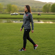Woman walking on grass wearing a gray jacket and black pants with red accents.
