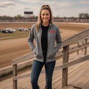 Woman standing on a wooden platform at a race track wearing a gray jacket with a red racing daughter heart design.