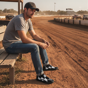 Man sitting on a wooden bench at a race track wearing checkered slip on shoes