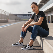 Woman sitting on a race track wearing black and white checkered slip-on shies.