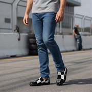 Person wearing blue jeans and black and white checkered shoes on a road.