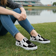 Woman wearing black and white checkered shoes sitting on grass by a lake.