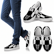 Black and white checkered slip-on shoes with glittery accents worn with blue jeans on a white background.