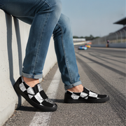 Person wearing black and white checkered shoes with blue jeans on a race track.